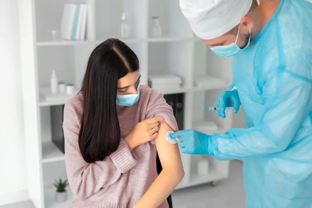 A smiling clinician in green scrubs rests a reassuring hand on the shoulder of an older female patient.