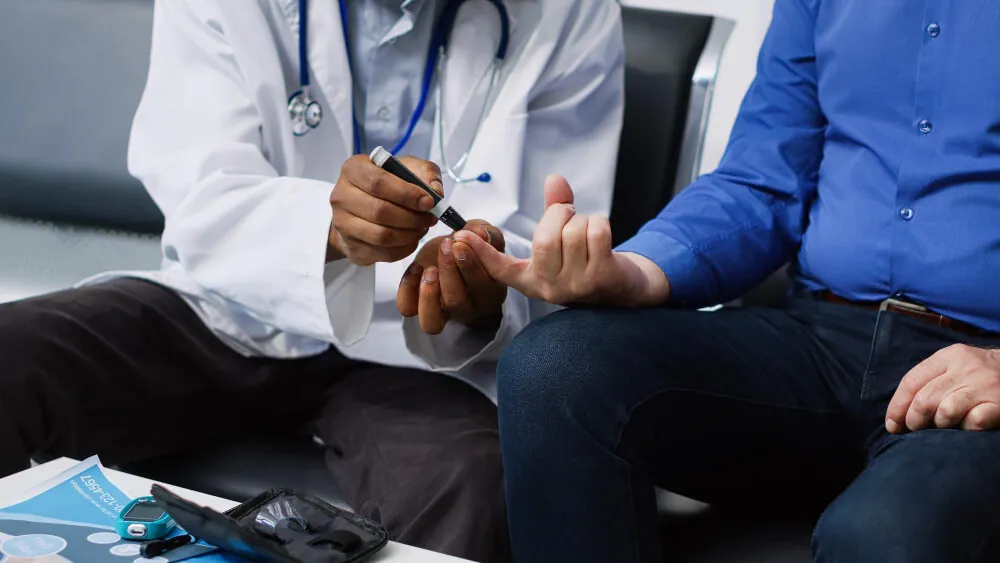 A nurse checks an older man’s blood pressure with a cuff while he sits on a sofa.