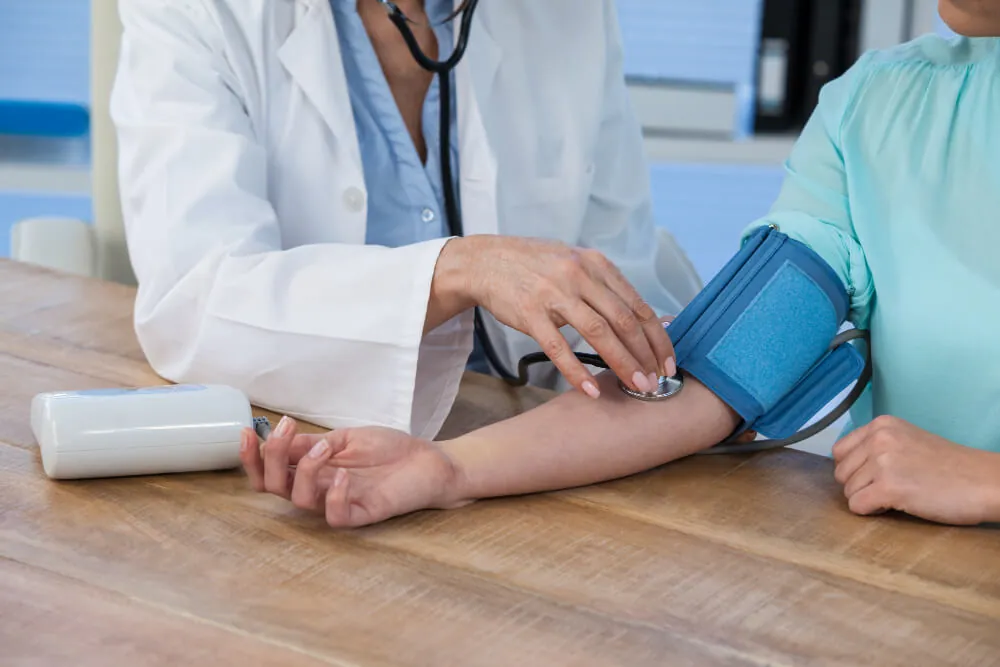 A nurse checks an older man’s blood pressure with a cuff while he sits on a sofa.