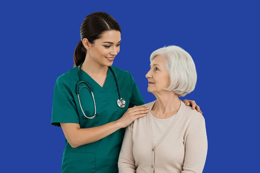 A smiling clinician in green scrubs with a stethoscope rests a reassuring hand on the shoulder of an older female patient.
